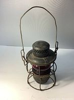 Front and side view showing handle, top embossing, wire cage, and red glass globe.