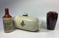 Three stoneware pottery items: Clayton's ginger beer bottle, Royal Doulton foot warmer, and handcrafted signed vase against white background.