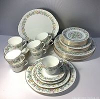 Full overview of all items in the lot showing stacked plates, cups, saucers and cake plate.