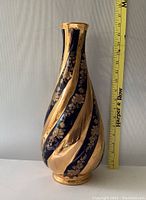 Side view showing twisted swirling gold and cobalt blue bands with flower patterns, and measuring tape for scale