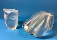 Two satin glass paperweights on blue background, owl on left, abstract wave on right