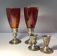 Two pairs of sterling silver candle holders, shorter plain pair in front, taller with etched red glass shades behind