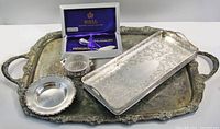 Photo showing all items in the lot including the large ornate silver plated copper tray, rectangular tray, boxed butter spreader and sugar spoon, sterling silver condiment dish with glass insert, and sterling silver butter dish.