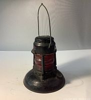Front view of the black metal lantern with red globe, standing upright with extended handle.