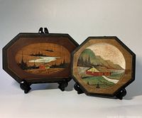 Two hand carved and painted wood plaques displayed on stands, showing full frontal views with visible round painted scenes and octagonal borders.
