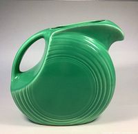 Side view of vintage green Fiesta Ware pitcher showing circular disc shape and concentric rings detail.