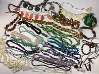 Overview photo of the entire lot showing multiple necklaces laid out flat with different colored stones and glass beads.