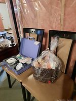 Overall view showing two chairs, one holding a purple case with the Optima electric body toner and the other holding a large cellophane wrapped basket with assorted beauty items.