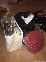 Overview photo showing three bedding items: rolled comforter in plastic, black bag with white bedding, maroon blanket wrapped in plastic.