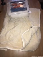 Photograph showing packaged Milano Health Duvet along with the unfolded side of the double sided wool blanket, cream colored with fleece texture.