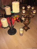 Full view of two candelabras with candles on floor, includes decorative fruit pieces and a glass candle holder with layered candle.