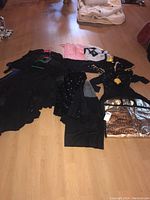 Assortment of ladies dance outfits laid out on floor showing multiple dresses and tops in black, pink, gold, and white.