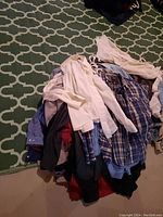 Pile of tangled men's dress shirts in various colors and plaid patterns on a carpeted floor.