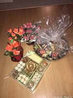 Photo showing two pots of faux flowers, a boxed assortment of candles and holders, and a wrapped Christmas gift basket.
