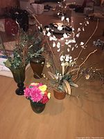 Four faux flower arrangements with vases placed on wooden floor in basement setting