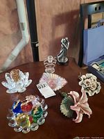 View of full lot on a wooden surface showing ceramic flowers, glass plate with colorful figurines, silver-tone couple figurine, crystal floral decors