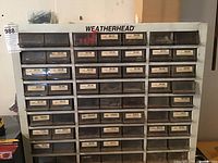 Front view of metal hardware organizer with 63 labeled plastic drawers with hardware inside, branded Weatherhead.