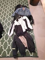 Six jackets laid out on a green patterned carpet. Includes a light blue Levi's jean jacket size M, black and white Puma jacket, and other black jackets.