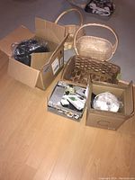 Overview of three baskets, electric rice cooker, alligator chopper set in boxes, all on floor.