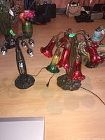 Two table lamps on the floor, one with red and green glass floral shades on curved arms, another with multiple bulb holders missing shades.