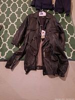 Two black leather jackets on the floor, showing front view, pockets, collars, and inner lining