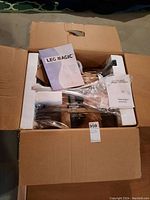 Opened box containing Leg Magic exercise equipment with visible foot platforms, handlebar, and protective styrofoam.