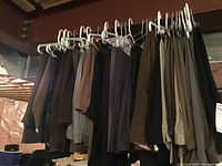 Men's dress pants hanging on hangers viewed in a row showing assortment of colors including dark and tan.