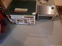 Wolfgang Puck pressure oven alongside its original cardboard box displaying brand and model information.