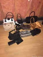 Photo of eleven handbags, purses, and wallets of varying colors and styles arranged on a wooden floor against a pinkish wall.