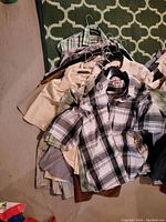 Photo showing a pile of men's short sleeve shirts in various colors and patterns on hangers arranged on the floor.