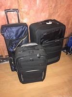 Three black suitcases piled together showing their sizes and handles; two have wheels and telescoping handles.