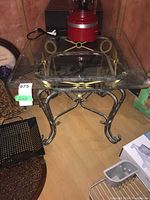 Full view of metal table with glass top, showing square glass surface and gold-accented metal legs.