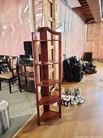 5 tiered wood corner shelf with five shelves and a decorative top handle, in a basement area with unfinished walls.