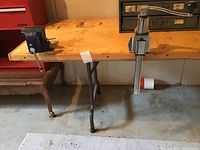 View of the left side of the folding work table showing attached blue metal vice and wooden top with signs of use.