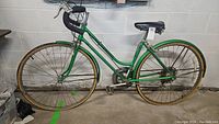 Side view of vintage green Schwinn Suburban bike showing flat yellow-sidewall tires, step-through frame, white saddle, and rust on metal parts.