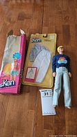 Top view of open original Ken doll box, unopened Ken clothing blister pack, and Ken doll dressed in blue shirt and jeans