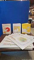 Wide shot of multiple Beatrix Potter children's storybooks and smaller books arranged on a table; shows book covers and colorful illustrations.