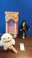 Harry Potter doll, Hedwig plush, and themed box on wooden surface with blue background.