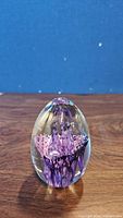 Front angle photo of the clear glass egg showing purple floral and swirl design inside on a wooden surface with blue background.