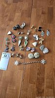 Lot of vintage clip-on earrings all laid out on a hardwood floor showing a variety of styles and colors including floral, geometric, and decorative designs with multiple materials.