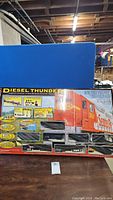 Box of Diesel Thunder electric train set displayed on floor showing locomotive, cargo cars, and farm accessories with summary of contents.