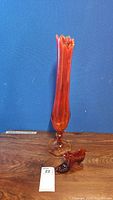 Tall amberina glass vase with scalloped rim and hexagonal base against blue background