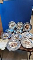 Set of 10 pewter plates themed around the American Revolution, some wrapped in plastic protective covers and others unwrapped, displayed leaning against a blue backdrop.