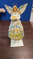Front view of Jim Shore angel figurine showing female figure with wings, halo, and holding seashells.