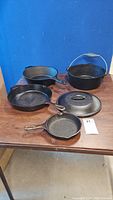 Full set of four black cast iron cookware pieces on a wooden table against blue background.