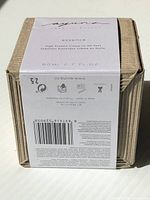 Front view of the packaging showing product name, brand, and volume information on a white label wrapped around a textured cardboard box.