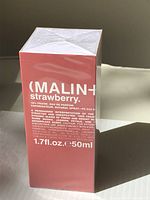 Photo of the front side of the pink box of Malin + Goetz Strawberry Eau de Parfum showing product details and size (1.7 fl. oz / 50ml), sealed in plastic wrap.
