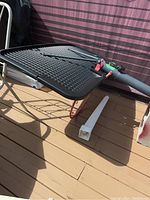 Black rectangular backboard with pink border, white square target, red metal rim attached with chain loops, and grey support pole lying on a deck.
