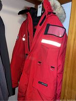 Red parka hanging on hanger showing front, hood and sleeve pocket