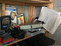 Shelf containing Mastercraft drill bit sets, a metal tool box, Husky nailer, and other tools.